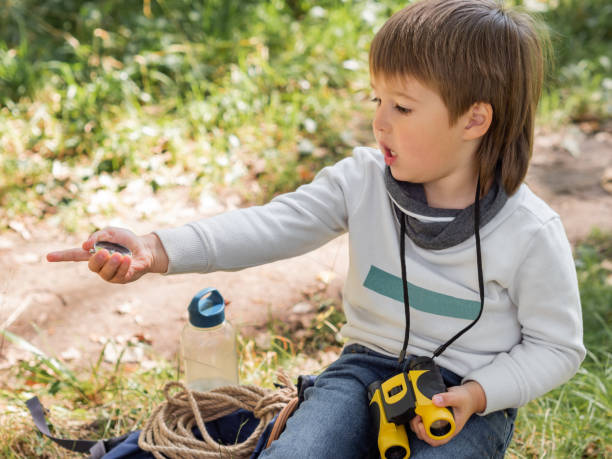 istock Little explorer on hike in forest. Boy with binoculars and compass sits on stump and reads map. Outdoor leisure activity for children. Summer journey for young tourist. 1283529745