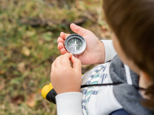 istock Little explorer on hike in forest. Boy with binoculars and compass sits on stump and reads map. Outdoor leisure activity for children. Summer journey for young tourist. 1283529826