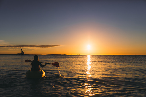 Young woman tourist feeling awe and freedom kayaking in the Inidan ocean during the picturesque sunset on Zanzibar, Tanzania - East Africa