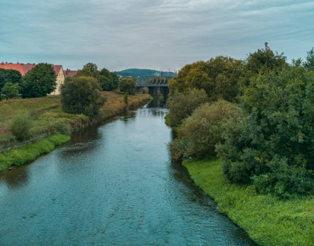 istock Cloudy Landscape of small river between bushes and trees with train bridge over it 1283537056