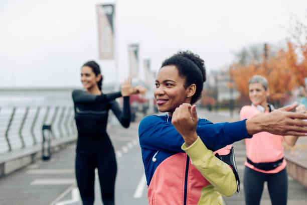 młoda kobieta i jej koledzy z drużyny rozgrzewają się na trening na zewnątrz - exercising stretching women outdoors zdjęcia i obrazy z banku zdjęć