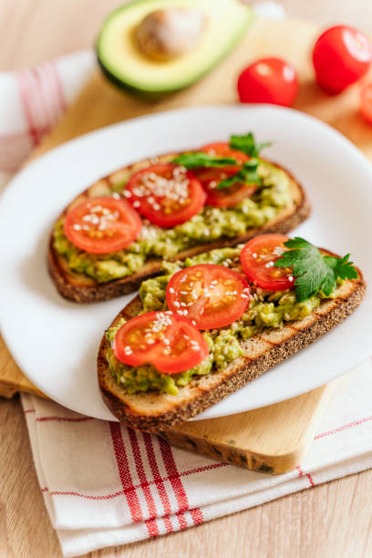 istock toasted bread with avocado paste and fresh tomato. Avocado mixed with lemon juice is spread on bread.  health food concept, vegan, vegetarian 1283542495