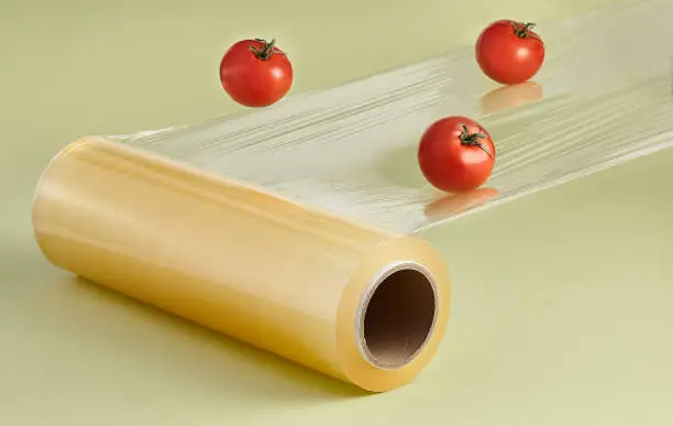 Roll of transparent film for wrapping food. Flying tomato. Creative minimal packing concept. Pastel green background