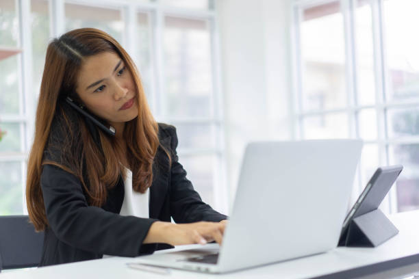 close up young secretary woman talking with partner and using tablet to make report or answer email to customer during opening digital tablet at office room for multitasking and busy working life concept
