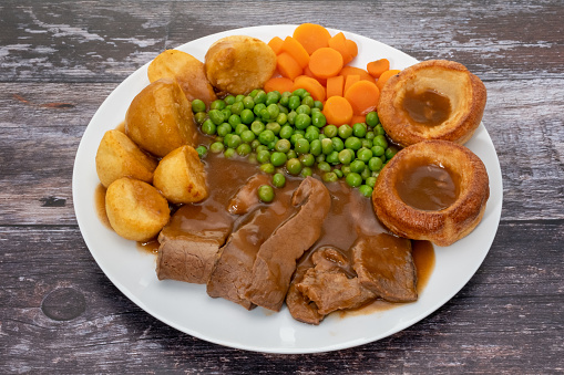 Traditional Sunday dinner of roast beef, roast potatoes, vegetables, and yorkshire puddings with gravy