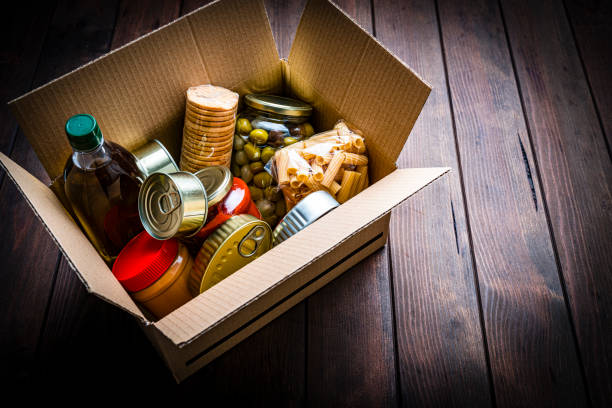 caja de cartón llena de alimentos no perecederos sobre mesa de madera. vista de ángulo alto. - non perishable fotografías e imágenes de stock