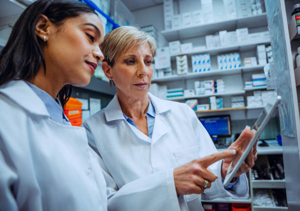 istock Elderly pharmacist guiding new female intern teaching scrolling on digital tablet standing in pharmacy 1283551129