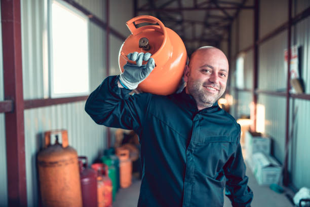 travailleur de sourire transportant la bouteille de gaz pour le remplissage - natural gas cylinder flammable fire photos et images de collection