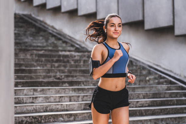 junge kaukasische läuferin joggen auf der treppe in sportlichen outfit im freien - joggen stock-fotos und bilder