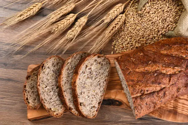Top view of a loaf of multi-grain bread on a cutting board with a burlap sack of grain and wheat stalks.