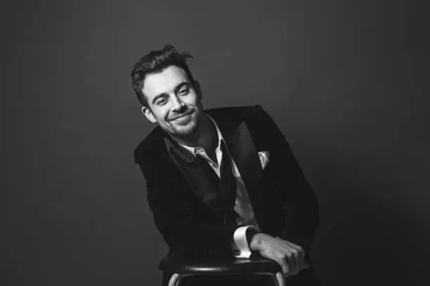 Studio portrait of a young caucasian man in a tuxedo, smiling, looking at the camera, against plain studio background