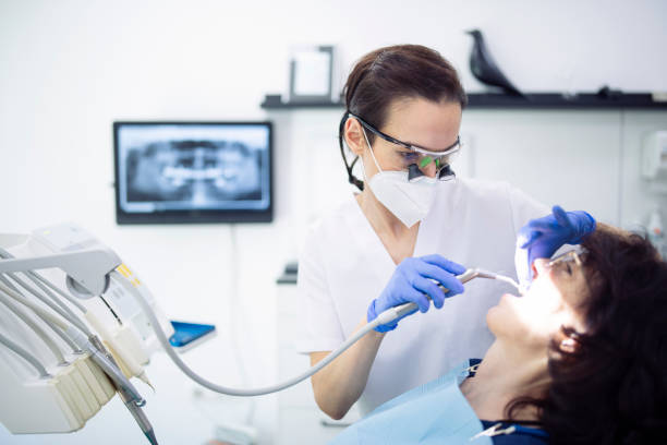Professional female dentist working on patient. Side view shot of professional female dentist working on patient teeth. surgical light stock pictures, royalty-free photos & images