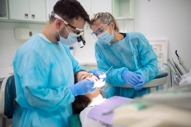 Dentist examining patient mouth in medical clinic. Dentist and her assistant working on young female patient in medical clinic with protective equipment, dental health during covid-19 pandemic. dental hygienist stock pictures, royalty-free photos & images