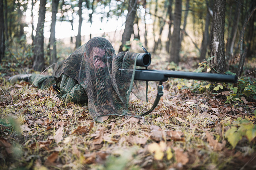 Hunter is hidden in the forest and shooting with sniper rifle, autumn hunting season.
