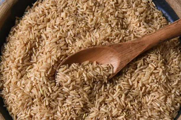 Closeup of a wooden spoon in a bowl full of brown rice.
