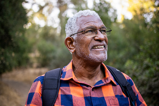 A senior black man with white hair hiking outdoors.