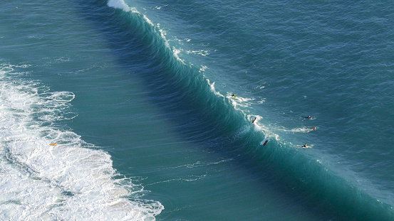 Body borders and surfers trying to ride dangerous breaking blue big wave in Nazare Portugal in aerial view from Miradouro do Suberco point