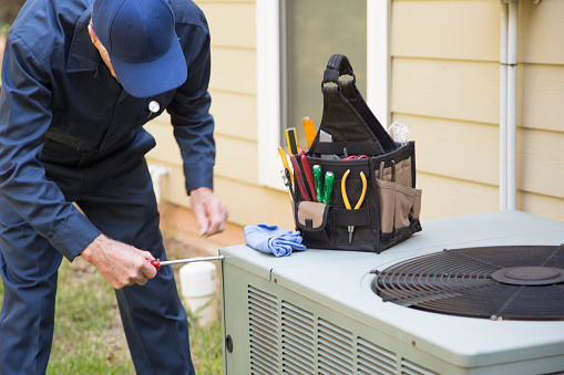 Senior Adult air conditioner Technician/Electrician  services outdoor AC unit and the Gas Generator.  He checks the oil in the generator.