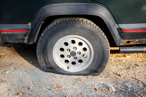 A SUV carwith a flat tire is seen parked on a dirt road.