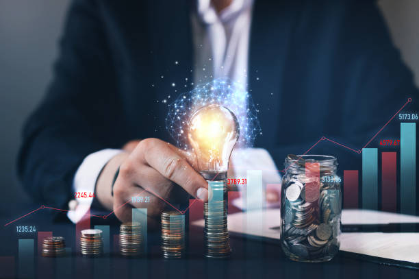 istock Businessman holding illuminated light bulb futuristic and stack of coins with gidital graph. Business innovation technology. 1283569471