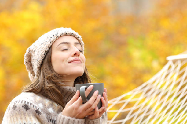 女性は秋にコーヒーカップを持って新鮮な空気を吸う