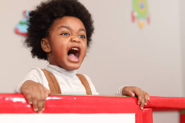 garçon afro-américain avec des cheveux bouclés criant tout en jouant à la cour de récréation, enfant ayant l’amusement sur le terrain de jeu. - crier photos et images de collection