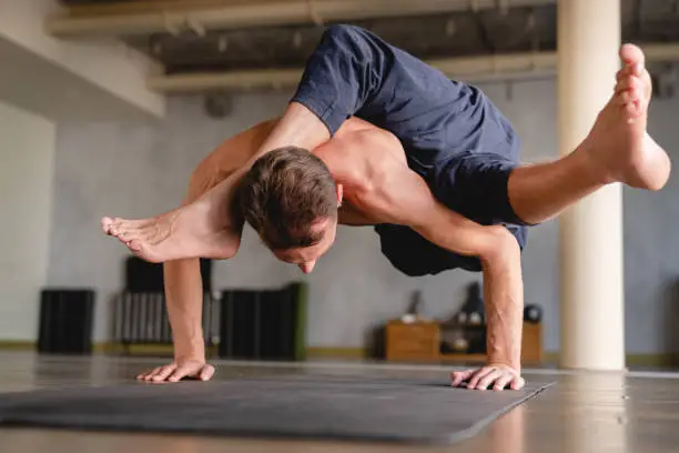 Strong male yogi standing on his hands with both feet in the air indoors