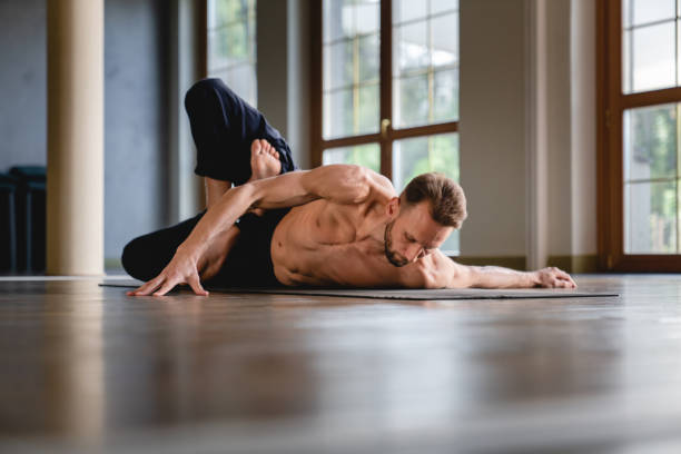 istock Handsome fit caucasian man in yoga position lying on the karemat while stretching inside spacious studio 1283571626