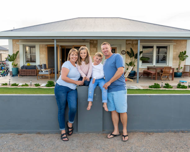 Outdoors portrait of a happy family of four smiling in front of new dream home or vacation rental house. Mom, dad, and children boy and girl, embracing and having fun together enjoying holiday villa. stock photo