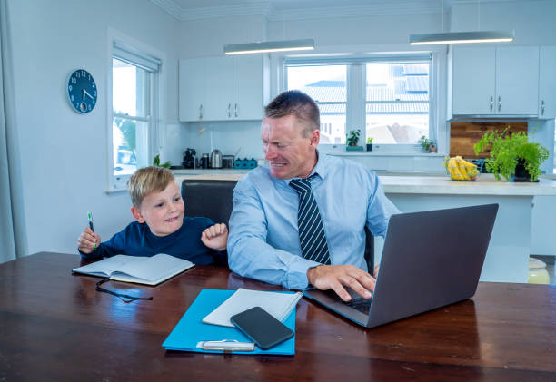 istock Stressed parent trying to cope with remote work and homeschooling. Man working from home while son child wants his attention. COVID-19 lockdown, quarantine, online learning and work from home concept. 1283574442