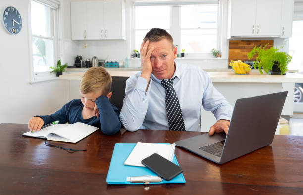 istock Stressed parent trying to cope with remote work and homeschooling. Man working from home while son child wants his attention. COVID-19 lockdown, quarantine, online learning and work from home concept. 1283574579
