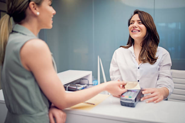 frau zahlt an einer rezeption in schönheitsbehandlungsklinik - healthcare and medicine receptionist paying credit card stock-fotos und bilder