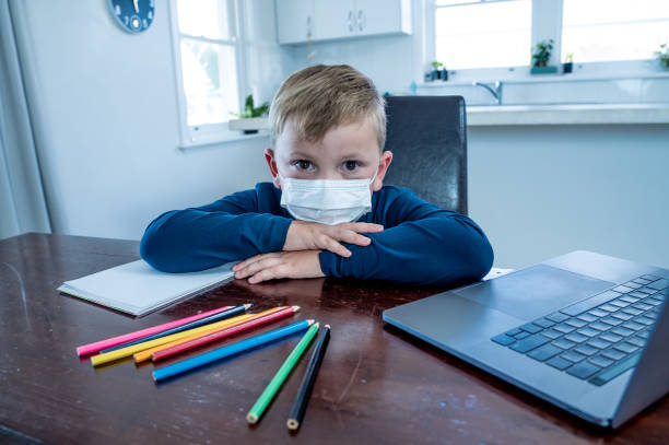 istock School boy with face mask watching virtual lesson in online education feeling bored and depressed at home in self-isolation. Remote learning and closed schools due to COVID-19 outbreak second wave. 1283577573