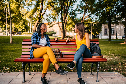 Two female multi-ethnic friends talking on a park bench.