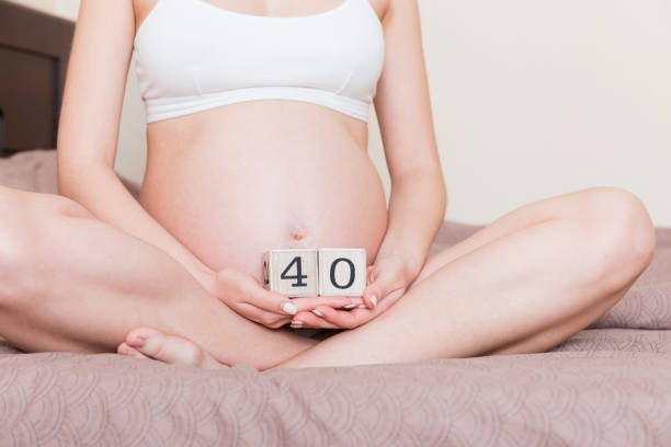 donna incinta in biancheria intima bianca a letto a casa che tiene il calendario con settimane 40 di gravidanza. concetto di maternità. in attesa di un bambino imminente - 40 weeks foto e immagini stock