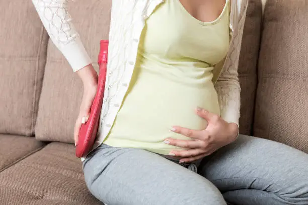 Pregnant woman suffer from back pain holds a hot bottle or warmer against her back. Concept pregnant woman lifestyle and health care.