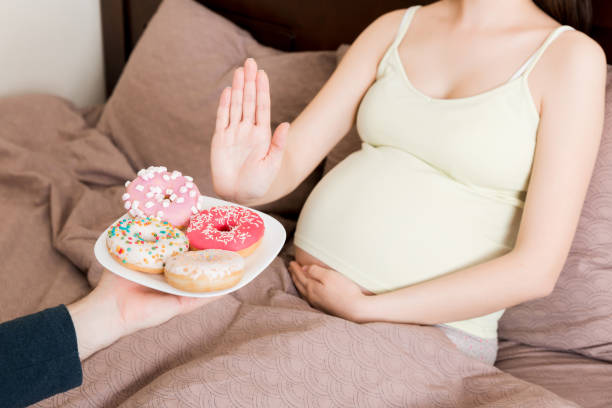 fermez-vous vers le haut de la femme enceinte restant dans le lit rejette pour manger la malbouffe telle que les beignets et ne fait aucun geste. alimentation saine pour le futur concept de mère - dieting food rejection women photos et images de collection