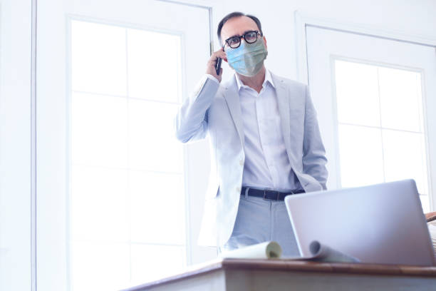 istock Latino Man Wearing Protective Face Mask Talking On Mobile Phone In HIs Office 1283581514