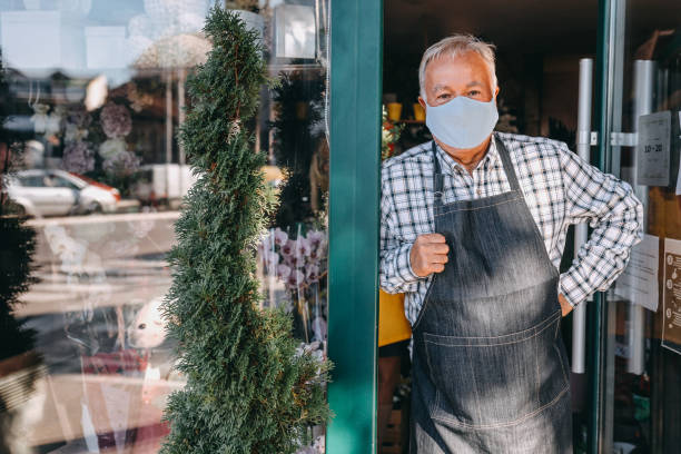 Man with protective face mask at entrance of flower shop Senior man florist with protective face mask at entrance of flower shop new normal concept stock pictures, royalty-free photos & images