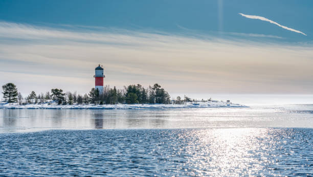 vue très proche du phare blanc rouge au milieu de l’île gelée et enneigée à la mer baltique froide, en partie en eau libre, glace mince reflétant la lumière du jour. ciel bleu, brise légère. nord de la suède, umea - frozen ice sky sun photos et images de collection