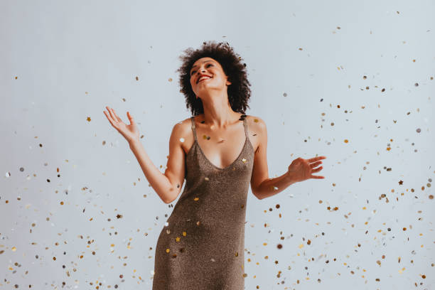 Happy Woman in a Gold Dress Dancing Under Confetti Smiling African American woman dancing under confetti, celebration concept (a portrait). carbonated photos stock pictures, royalty-free photos & images