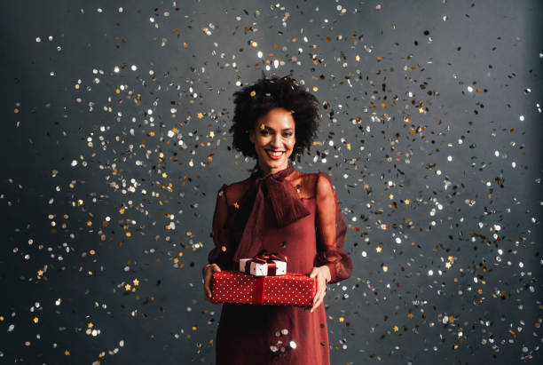 メリークリスマス:赤いお祝いのドレスを着た幸せなアフリカ系アメリカ人女性は、すべての周りを飛ぶ紙吹雪とクリスマスプレゼントを持って、肖像画
