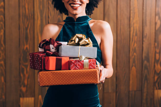 Merry Christmas: a n Anonymous Smiling Elegant African American Woman Holding a Pile of Presents in her Hands, a Close Up Retro celebration: a happy woman holding a lot of Christmas/birthday presents in her hands, feeling festive concept. stacked presents stock pictures, royalty-free photos & images