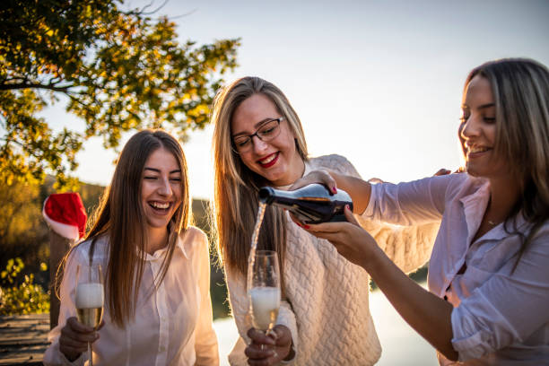 大晦日を祝う若い女性 - シャンパンで新年のお祝い - 若い女性、学生は、シャンパンを飲むことによって美しい自然の中で湖で新年を祝う - new years day new years eve new year ethnic ストックフォトと画像