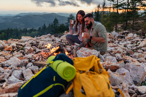 Two hikers sitting around fire and drinking coffee before they continue hike