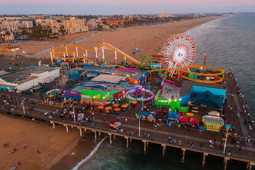 Santa Monica Pier at sundown with lights reflected in the Pacific Ocean with people enjoying the night