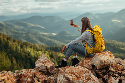 Young female with backpacker using phone while out on an adventurous in the mountains