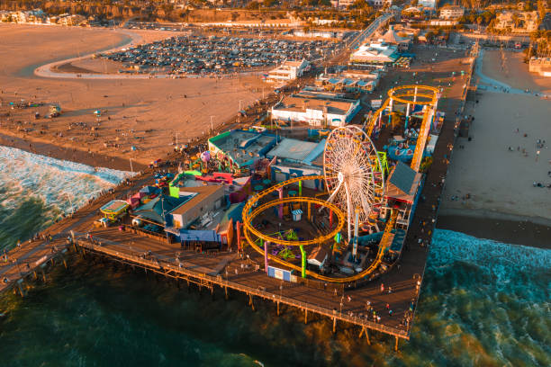 santa monica pier bei sonnenuntergang mit lichtern im pazifischen ozean reflektiert - santa monica city of los angeles los angeles county santa monica pier stock-fotos und bilder