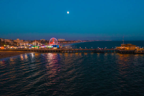 пирс санта-моника на закате с огнями, отраженными в тихом океане - santa monica pier santa monica beach night amusement park стоковые фото и изображения