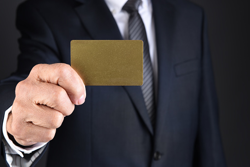 Closeup of a businessman holding a blank gold card in front of his toso. Man is unrecognizable.